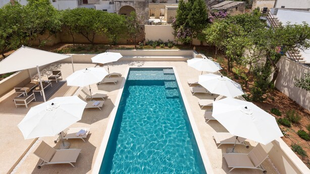 A rectangular swimming pool with clear blue water, surrounded by lounge chairs and white umbrellas. - Palazzo Fasti (Casarano)