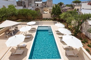 Une piscine rectangulaire à l’eau d’un bleu cristallin, entourée de chaises longues et de parasols blancs.