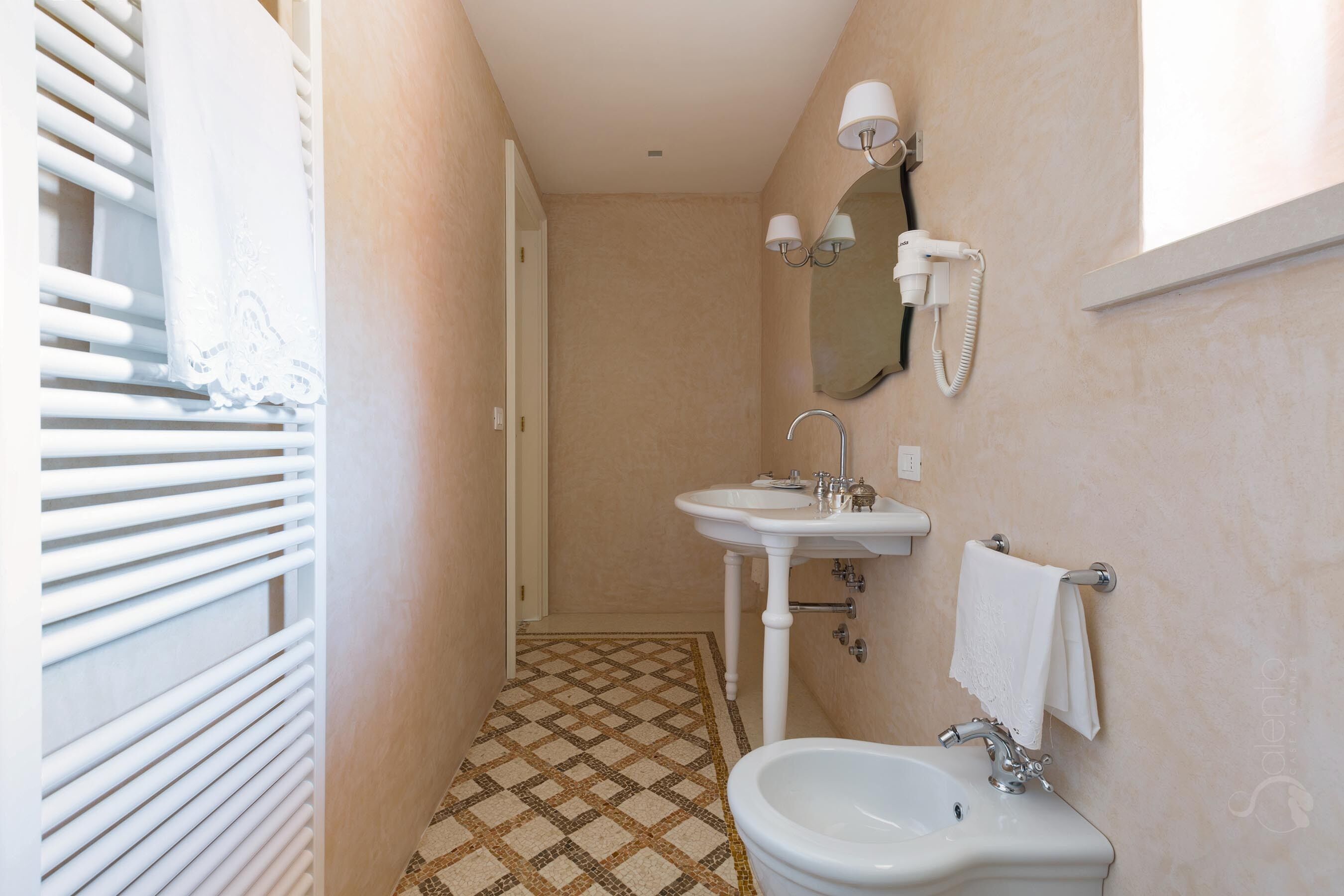Een kleine badkamer met betegelde vloer, een wastafel, een toilet en een spiegel.