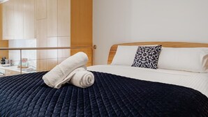 A hotel room with a bed, a wooden headboard, a white pillow, a patterned pillow, and a rolled white towel.