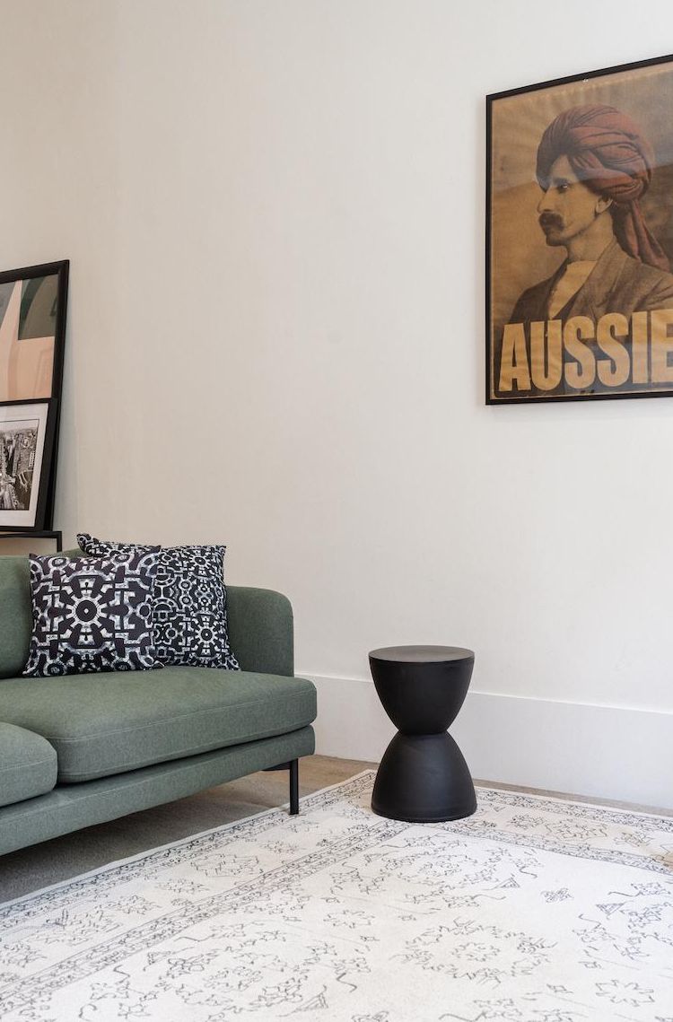 A room with a green sofa, a patterned throw pillow, a black round side table, and a poster on the wall.