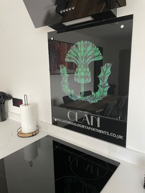 Une cuisine moderne dotée d’un pare-feu en verre, d’un porte-rouleau en papier et d’une plaque de cuisson à induction noire.