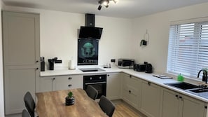Une cuisine compacte comprenant une table à manger, des chaises, un four à micro-ondes, une bouilloire et un évier.