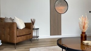 Ein modernes Wohnzimmer mit einer braunen Ledersofa, einem runden Spiegel, einem kleinen Beistelltisch und einer Vase mit Trockenpflanzen.