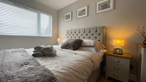 Ein ordentlich bezogenes Bett mit aufgerollten Handtüchern, einem gesteppten Kopfteil, Nachttischlampen und gerahmten Bildern an der Wand.