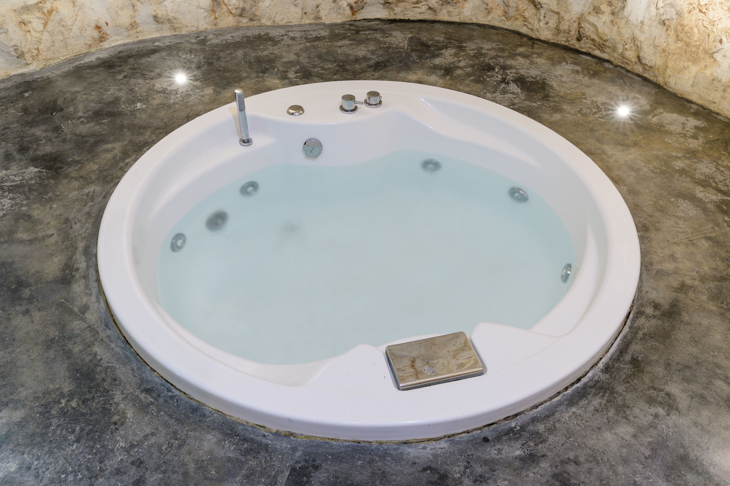 A round hot tub with a marble surround, a built-in seat, and a control panel with knobs and a faucet.