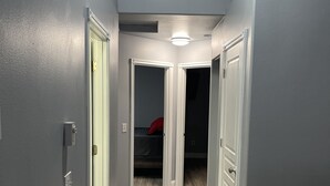 Un pasillo estrecho con paredes grises y suelo de madera, que conduce a un dormitorio con cama y un objeto rojo sobre ella.