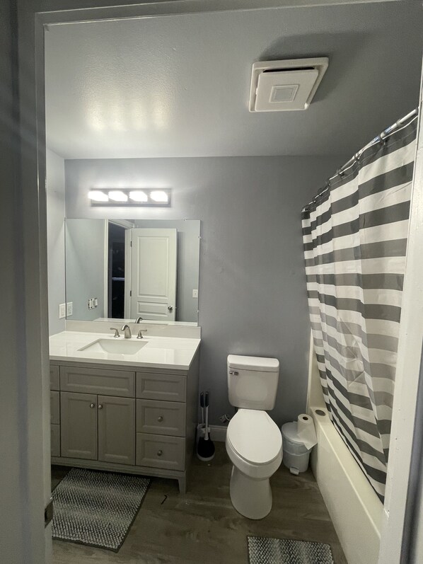 A bathroom with a white sink, mirror, and toilet. There is a striped shower curtain and a small trash can. - Multi-Family Condo - Sleeps 8 (Anchorage)