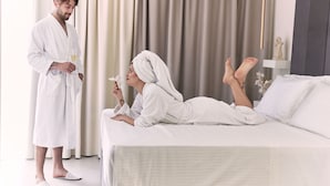 Une chambre d’hôtel avec un lit, une personne debout près de la fenêtre et une autre personne allongée sur le lit.