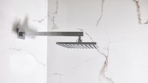 Une douche moderne dotée d’une poignée horizontale et d’un pommeau de douche à effet pluie, le tout fixé sur un mur en marbre blanc.