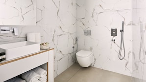 Une salle de bain avec un mur en marbre blanc, un lavabo blanc, des toilettes et une douche.