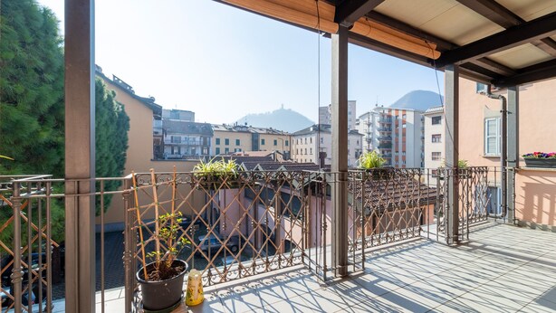 A balcony with a metal railing, potted plants, and a view of buildings and a mountain in the background. - Gerbett Apartment With Terrace by Wonderful Italy (Como)