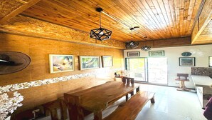 Een houten interieur met een lange eettafel, banken en hangende, geometrische lampen.
