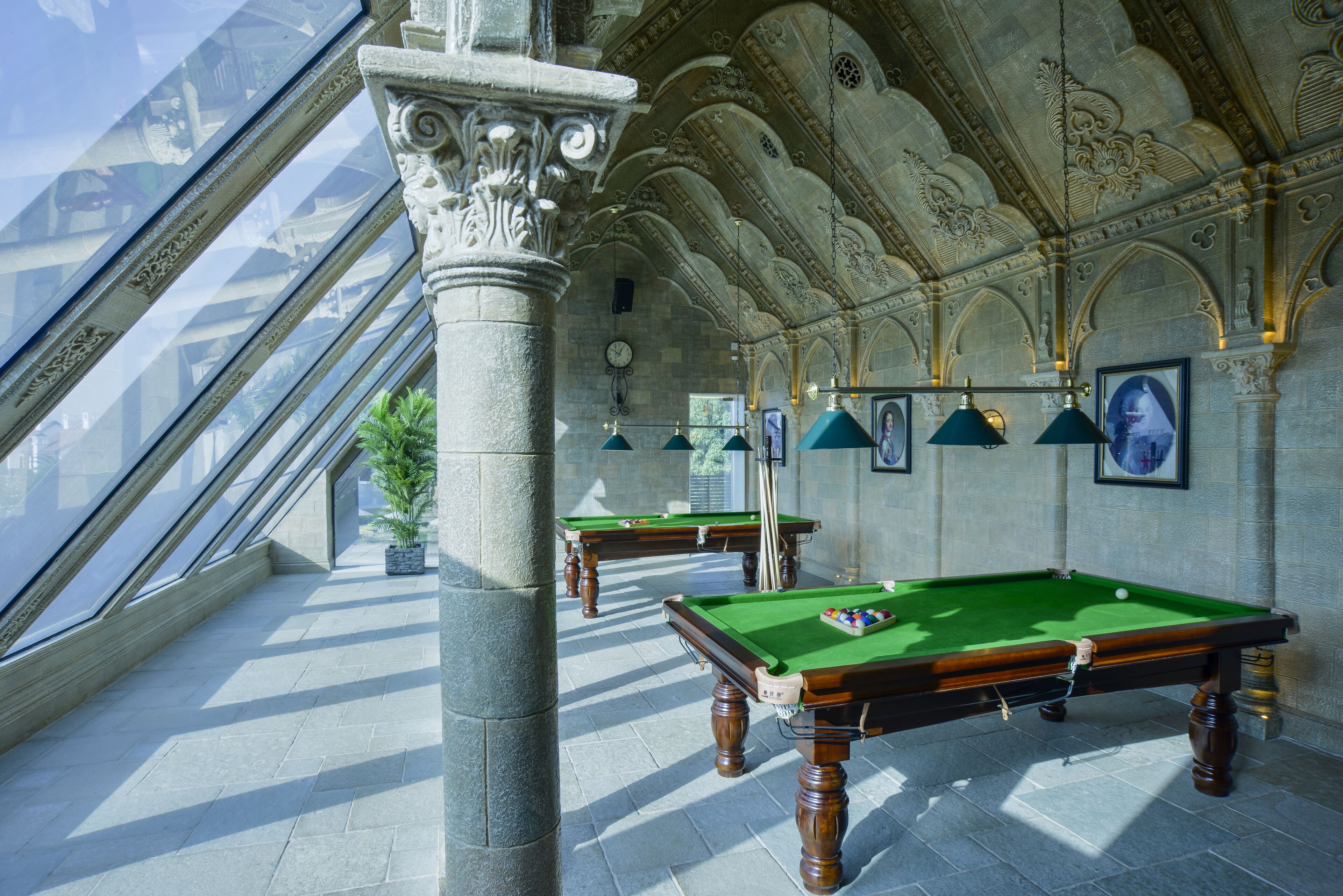 A billiards room with two tables, a large column, and a high ceiling with intricate designs.