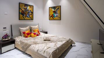 Une chambre à coucher moderne avec un grand lit, une table de chevet, un téléviseur et deux tableaux abstraits accrochés au mur.