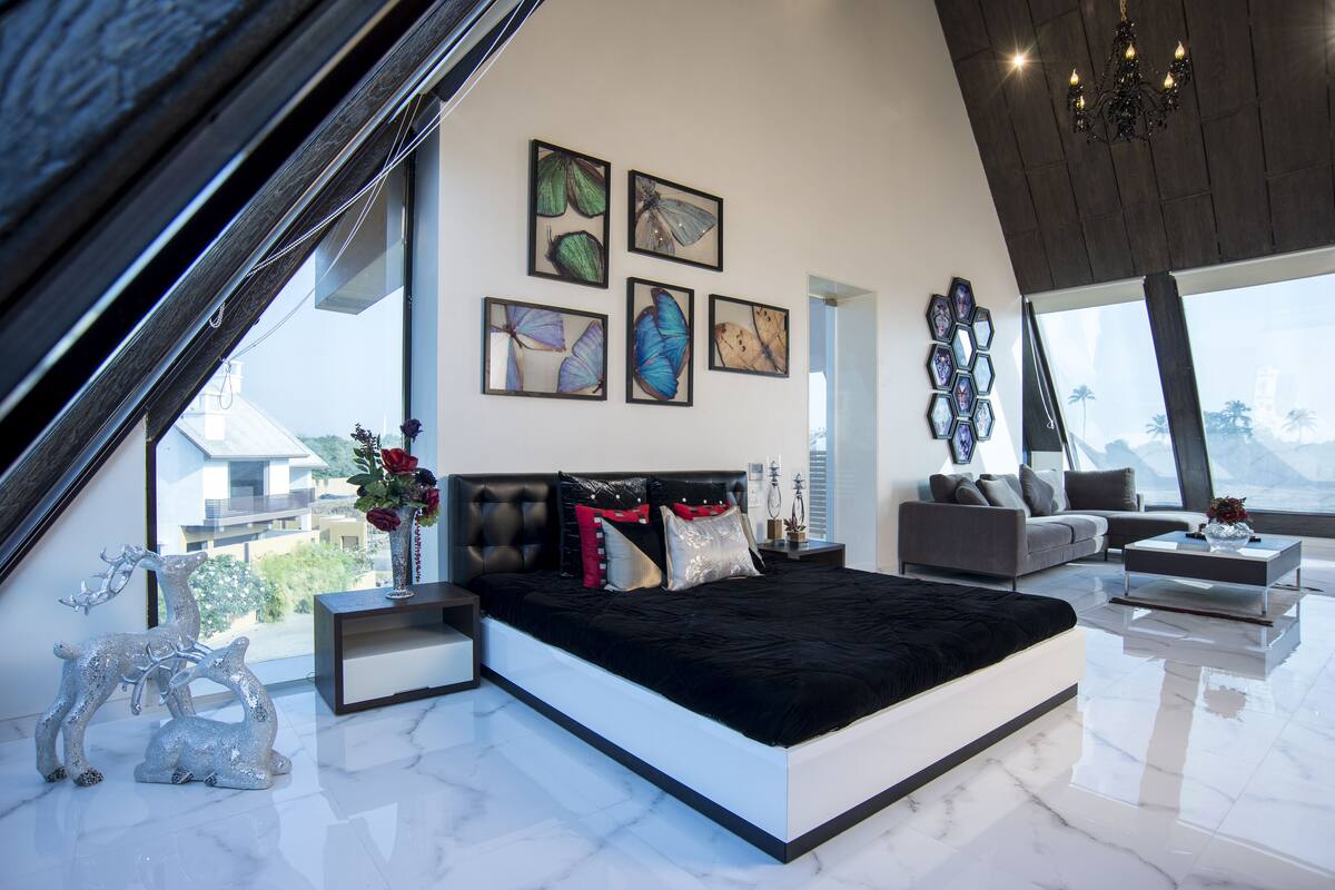A modern bedroom with a large bed, a sofa, and a coffee table. There are four framed butterfly pictures on the wall.