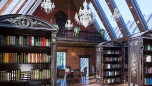 Una biblioteca amplia con techos altos, ventanas grandes y elaboradas estanterías de madera llenas de libros.