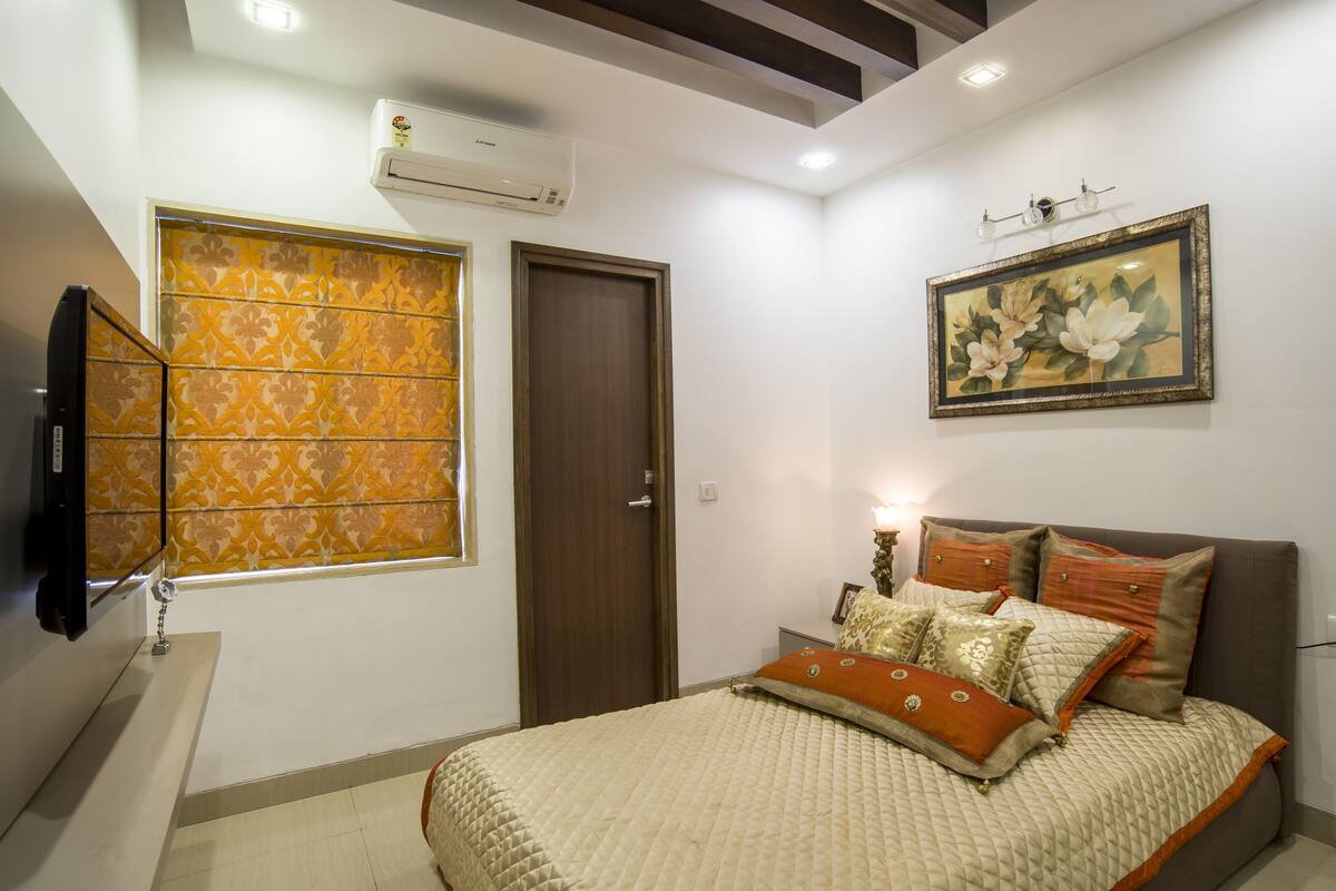 A bedroom with a bed, a window with patterned curtains, a door, and a wall-mounted air conditioner.