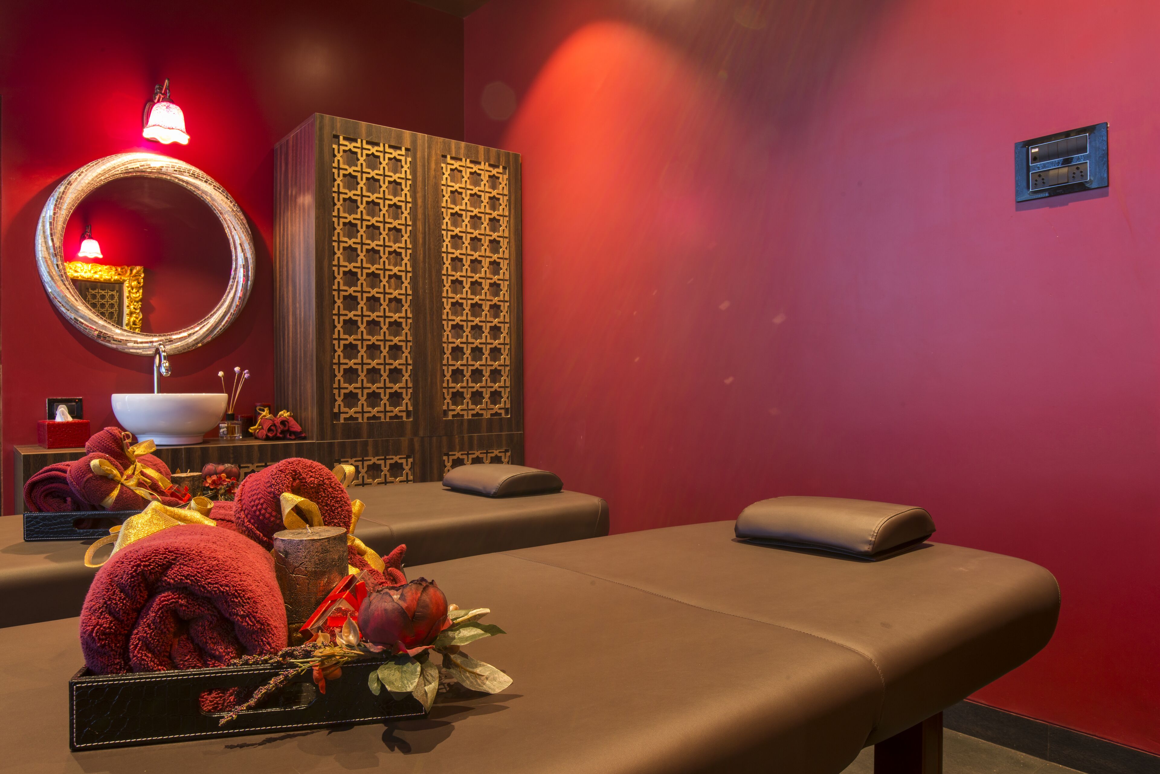 Une salle de soins avec une table de massage, un miroir décoratif, un meuble en bois et un petit lavabo.