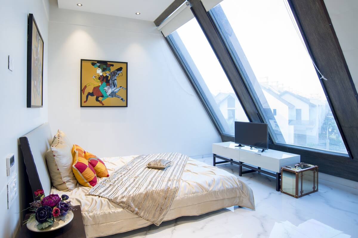 A modern bedroom with a large bed, a desk, and a skylight.