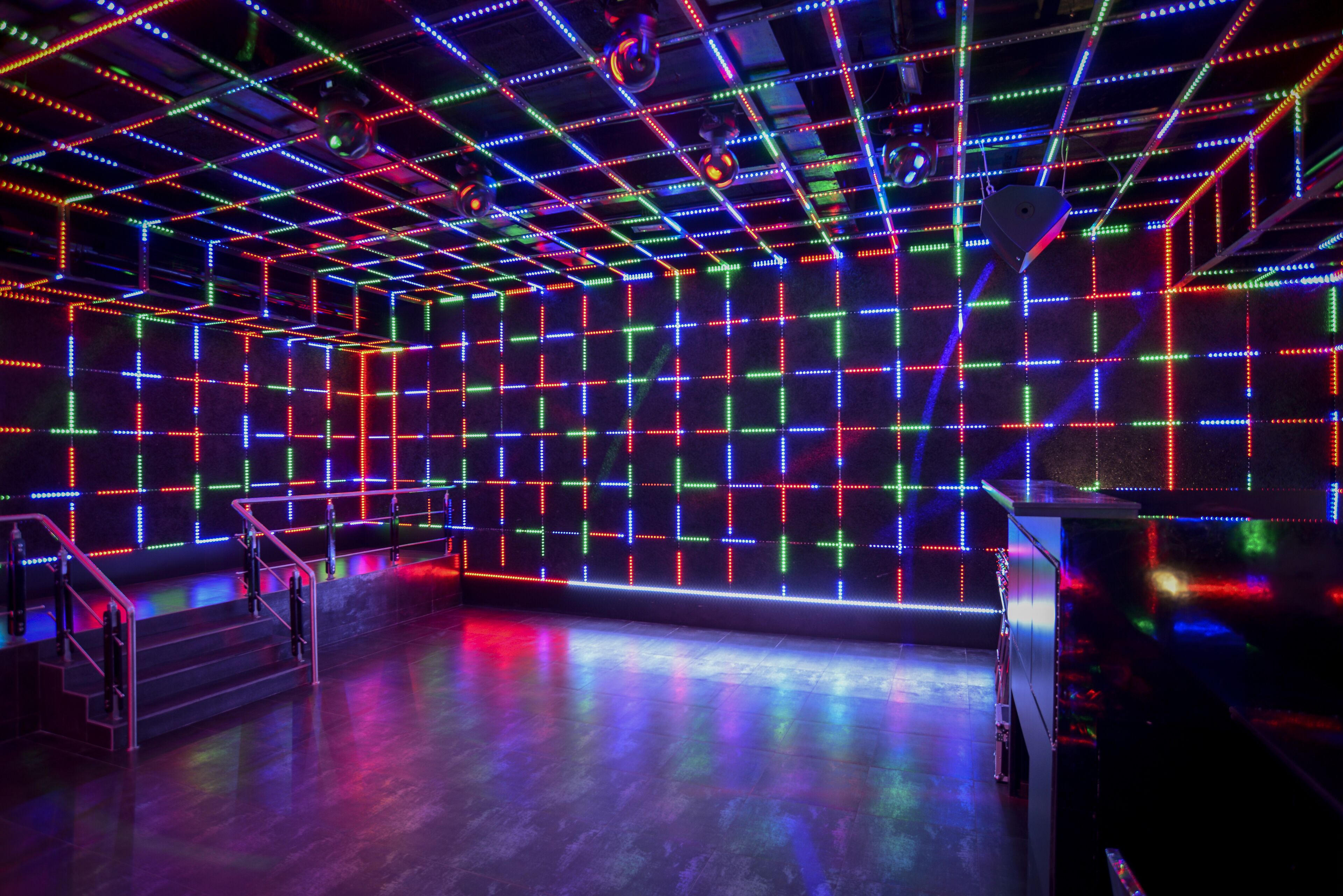 Una habitación con una cuadrícula de luces LED de colores en las paredes y el techo, una escalera y una plataforma.