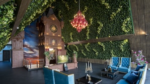 Un espacio de salón lujoso con una gran torre de reloj, asientos cómodos y un fondo de pared verde.