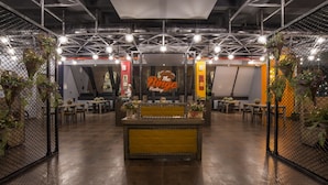 Un interior con un mostrador central, mesas, sillas y un letrero que dice "The Binge Factory".