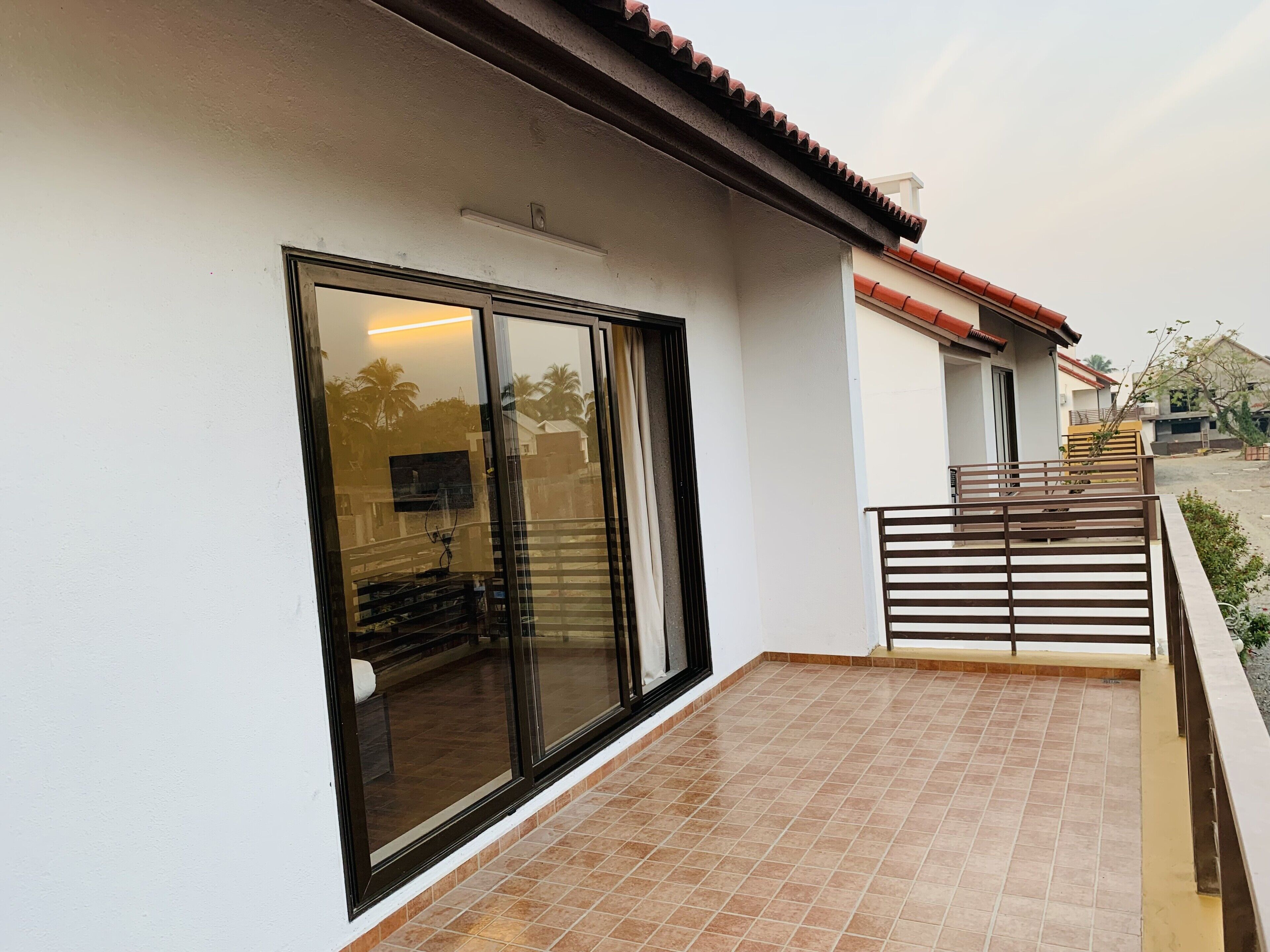 Une maison moderne dotée d’une grande porte-fenêtre coulissante, d’une terrasse carrelée et d’un petit balcon avec une rambarde en métal.