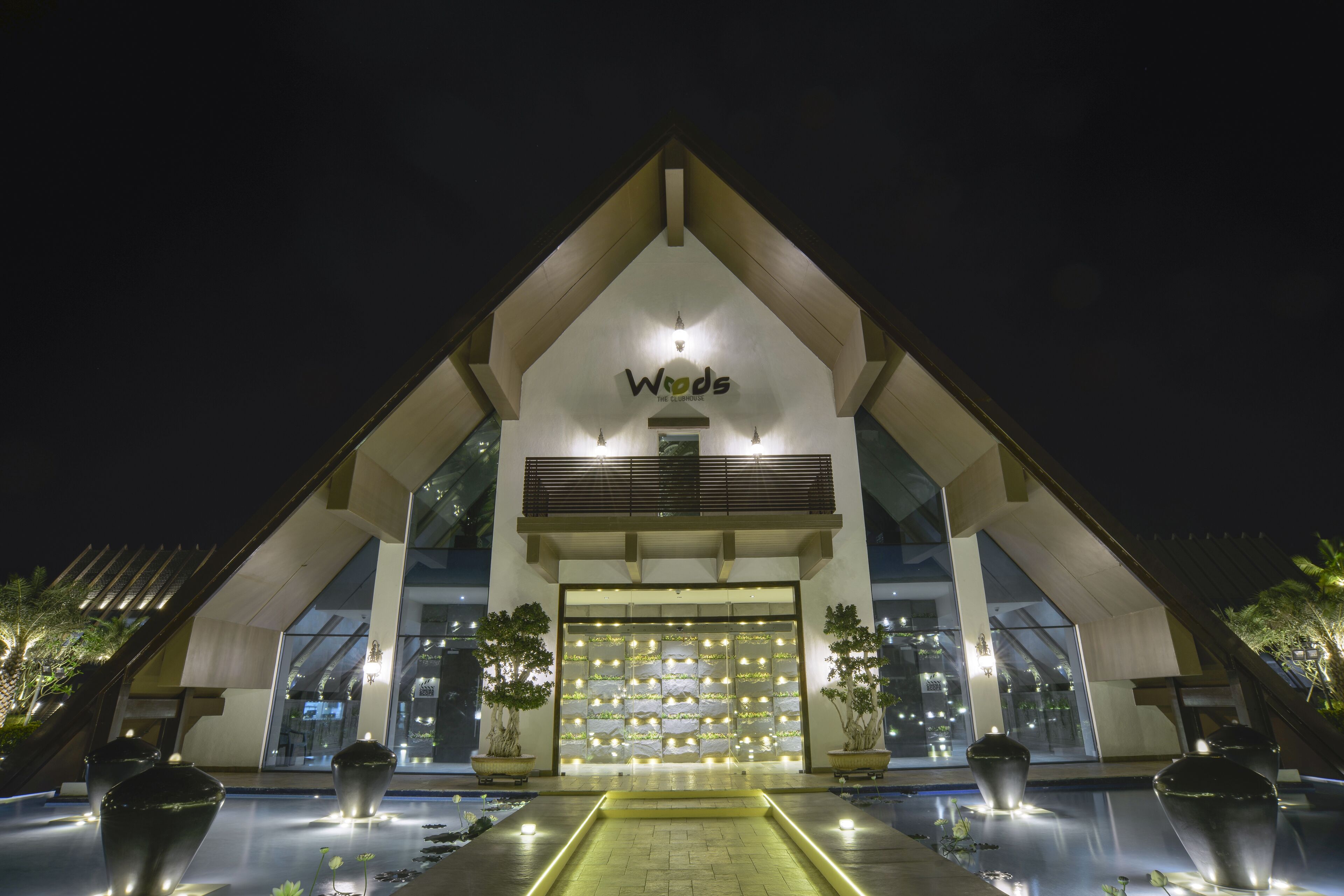 A modern hotel with a prominent 'Woods' sign, large windows, and a well-lit entrance area.