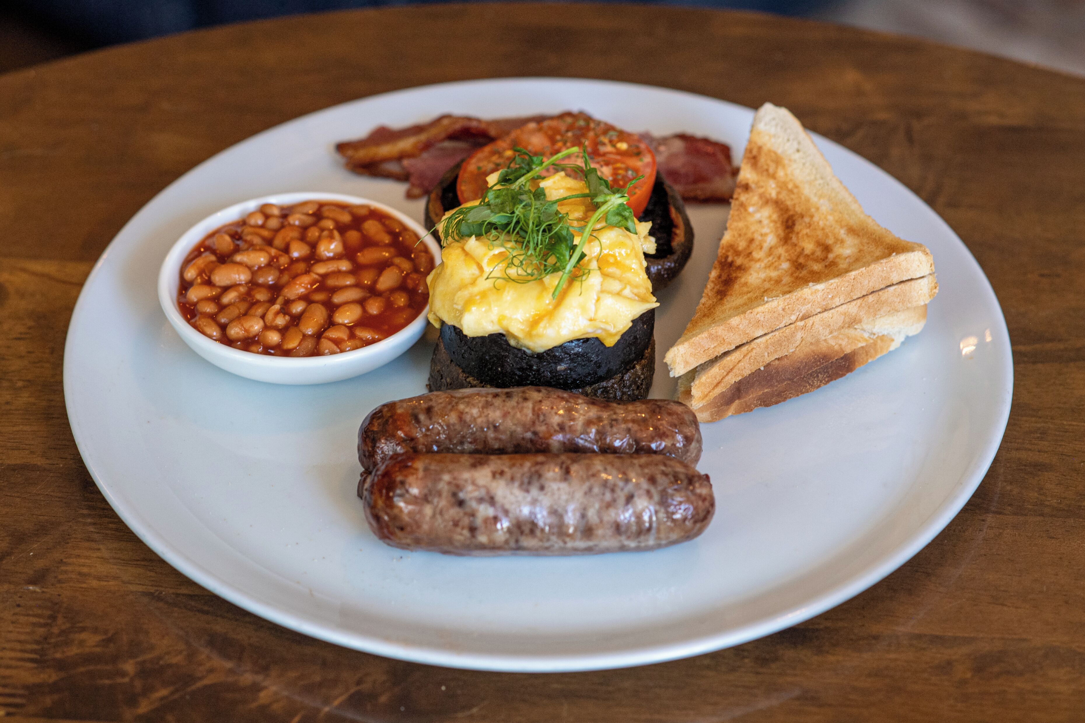Une assiette garnie de haricots, de saucisses, de pain grillé, d’œufs brouillés et de lardons.
