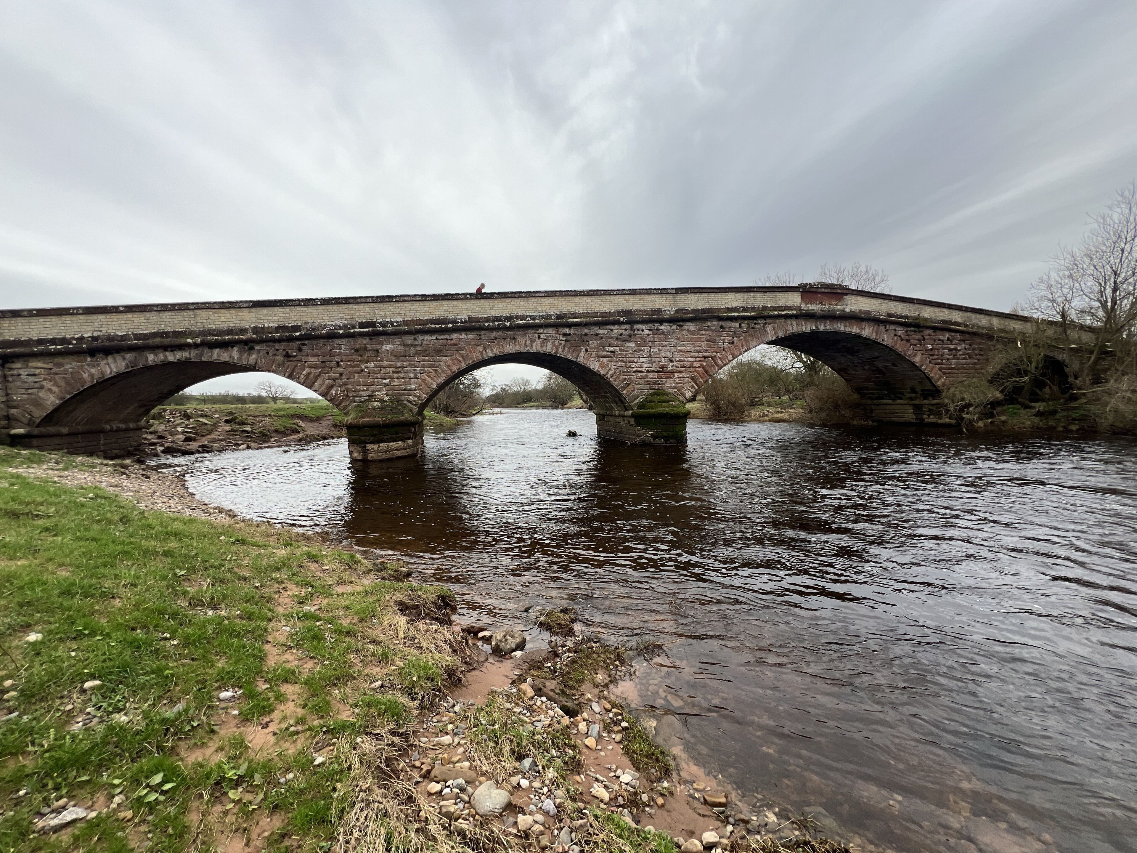 Un pont de pierre enjambant une rivière dont les berges sont couvertes d’herbe.
