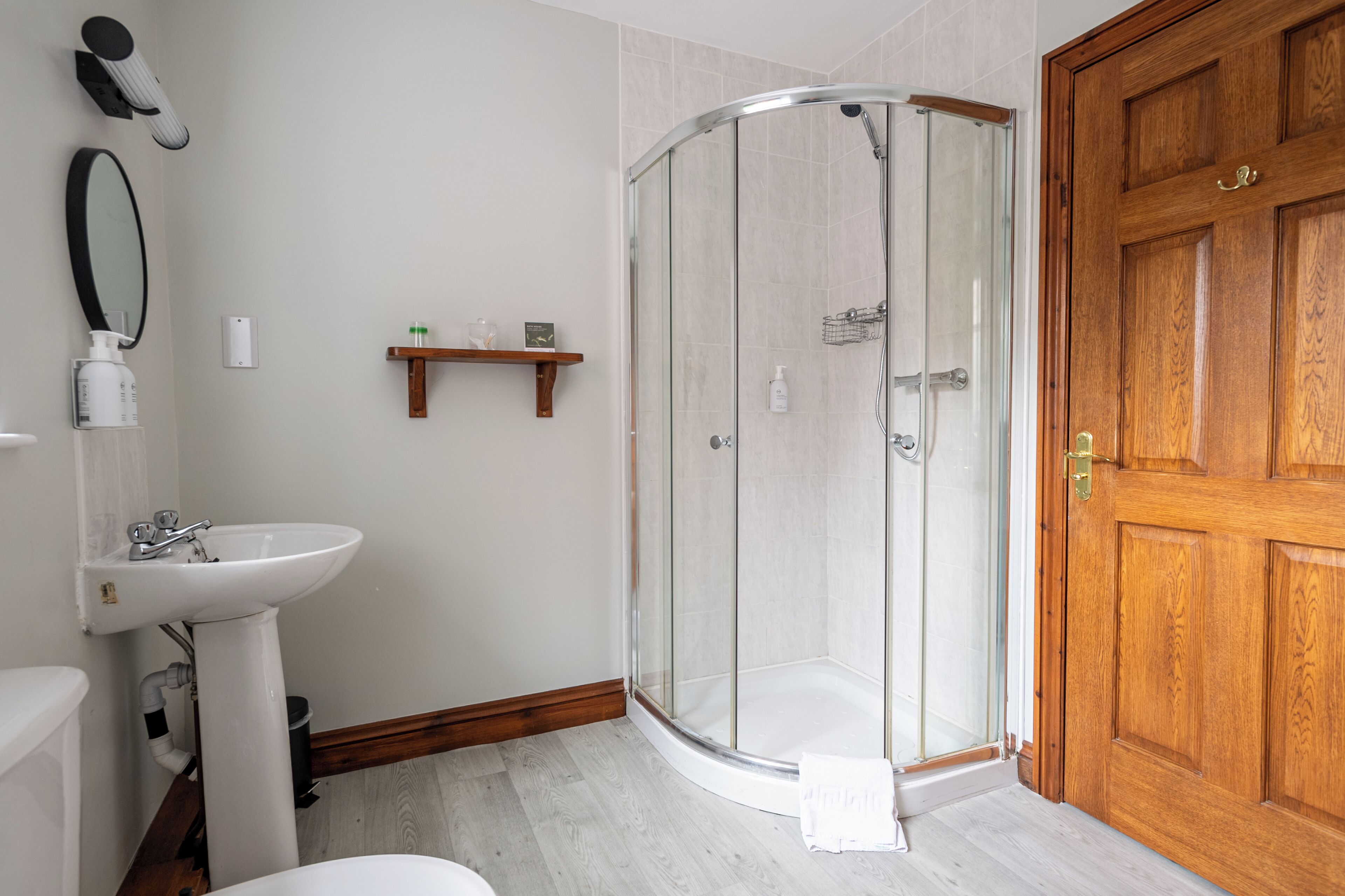 A bathroom with a glass-enclosed shower, a pedestal sink, and a wooden door.