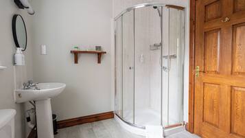 A bathroom with a glass-enclosed shower, a pedestal sink, and a wooden door.