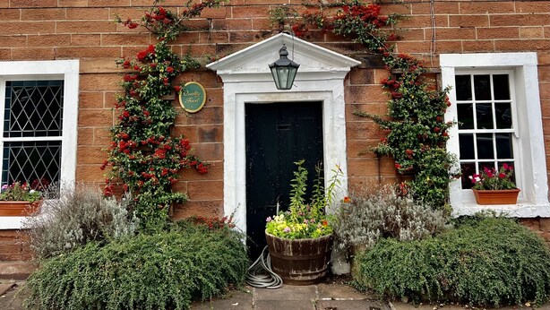 The Kings Arms Hotel with a brick facade, a central entrance with a black door, and flower boxes on either side. - The Kings Arms (Penrith)