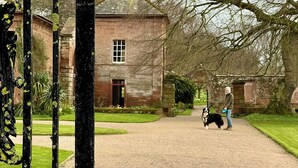 A historic building with a clock tower, a gravel path, and a dog walker with a dog. - The Kings Arms (Penrith)
