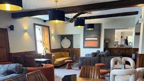 A spacious dining area with a wooden table and leather chairs, a bar area with stools, and a seating area with sofas and armchairs. - The Kings Arms (Penrith)