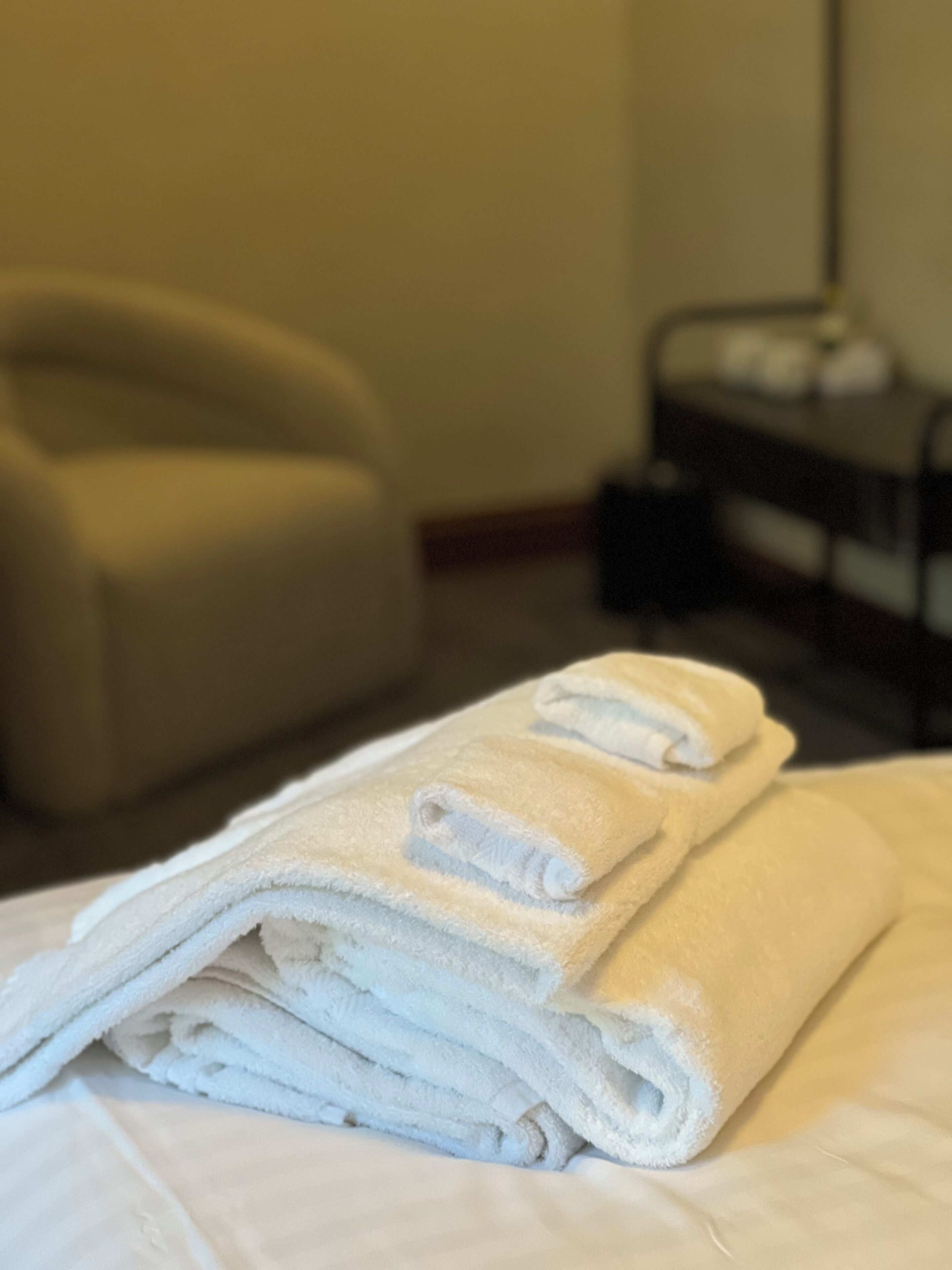 A neatly folded stack of white towels on a bed in a hotel room.