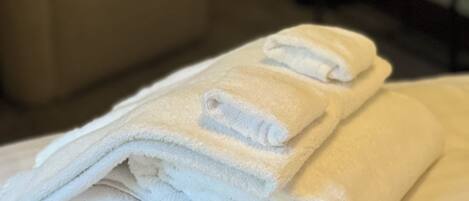 A neatly folded stack of white towels on a bed in a hotel room.