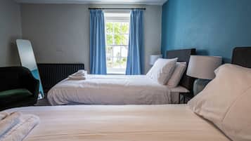 Una habitación de hotel con dos camas, una silla verde, una lámpara y una ventana con cortinas azules.