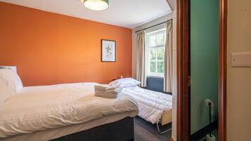 A hotel room with two beds, a framed picture on the wall, a window with curtains, and a radiator.