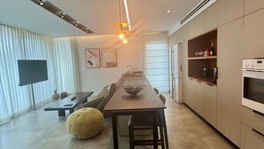 Une cuisine moderne dotée d’un îlot central, d’appareils électroménagers intégrés et d’un coin repas avec un canapé et un pouf.