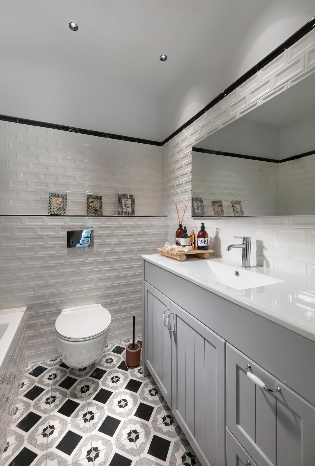 A modern bathroom with a white subway tile floor, a white toilet, a large mirror, and a white vanity with a sink.