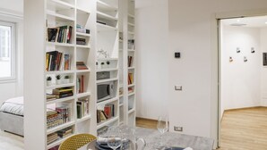 A modern living room with a white bookshelf, a dining table with chairs, and a bed. - Fuori Le Mura - Balcony & A/C (Como)