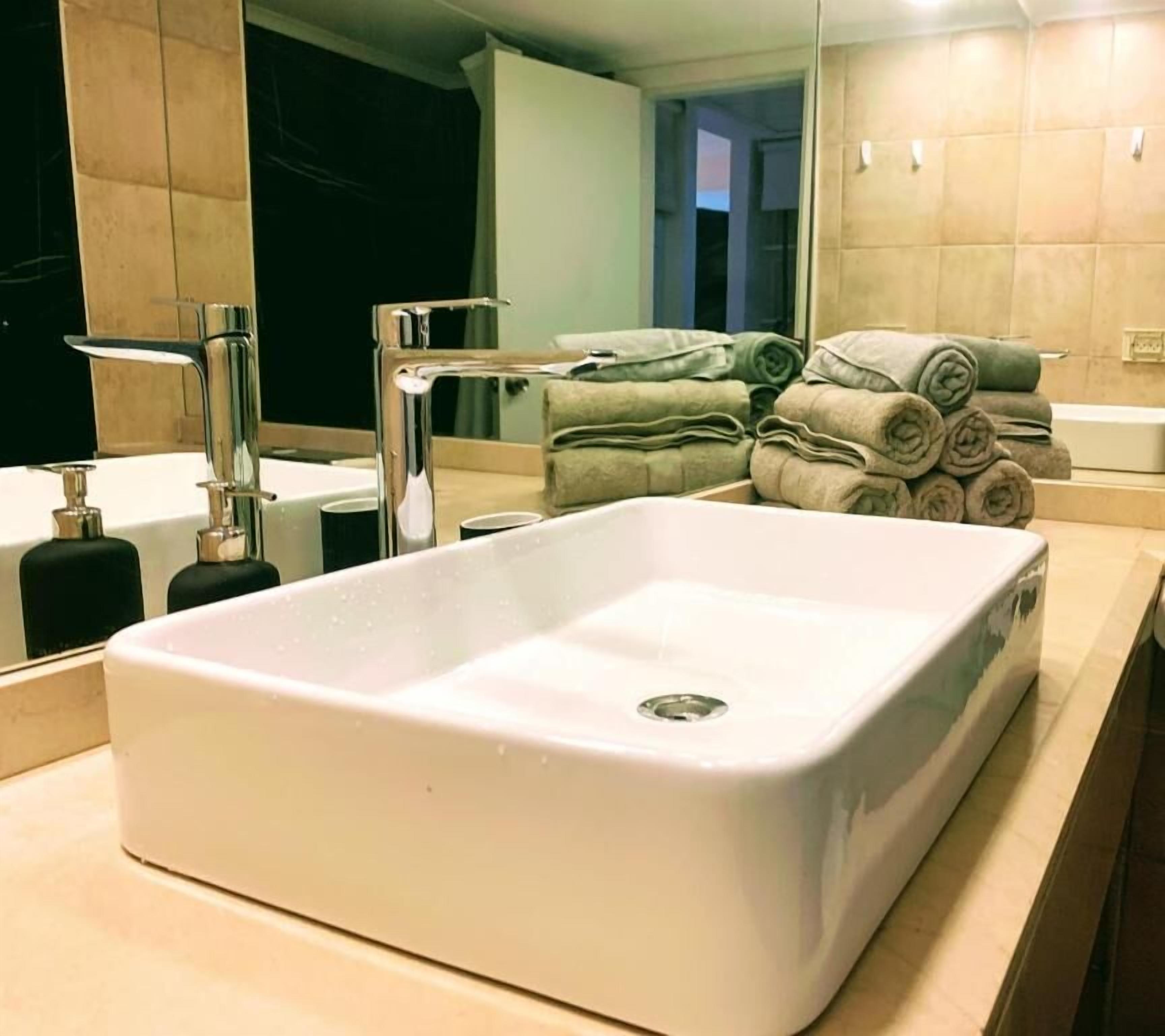 Un baño con un lavamanos blanco, un espejo y una pila de toallas.