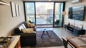 A modern living room with a sofa, a coffee table, a TV, and a balcony with a city view.