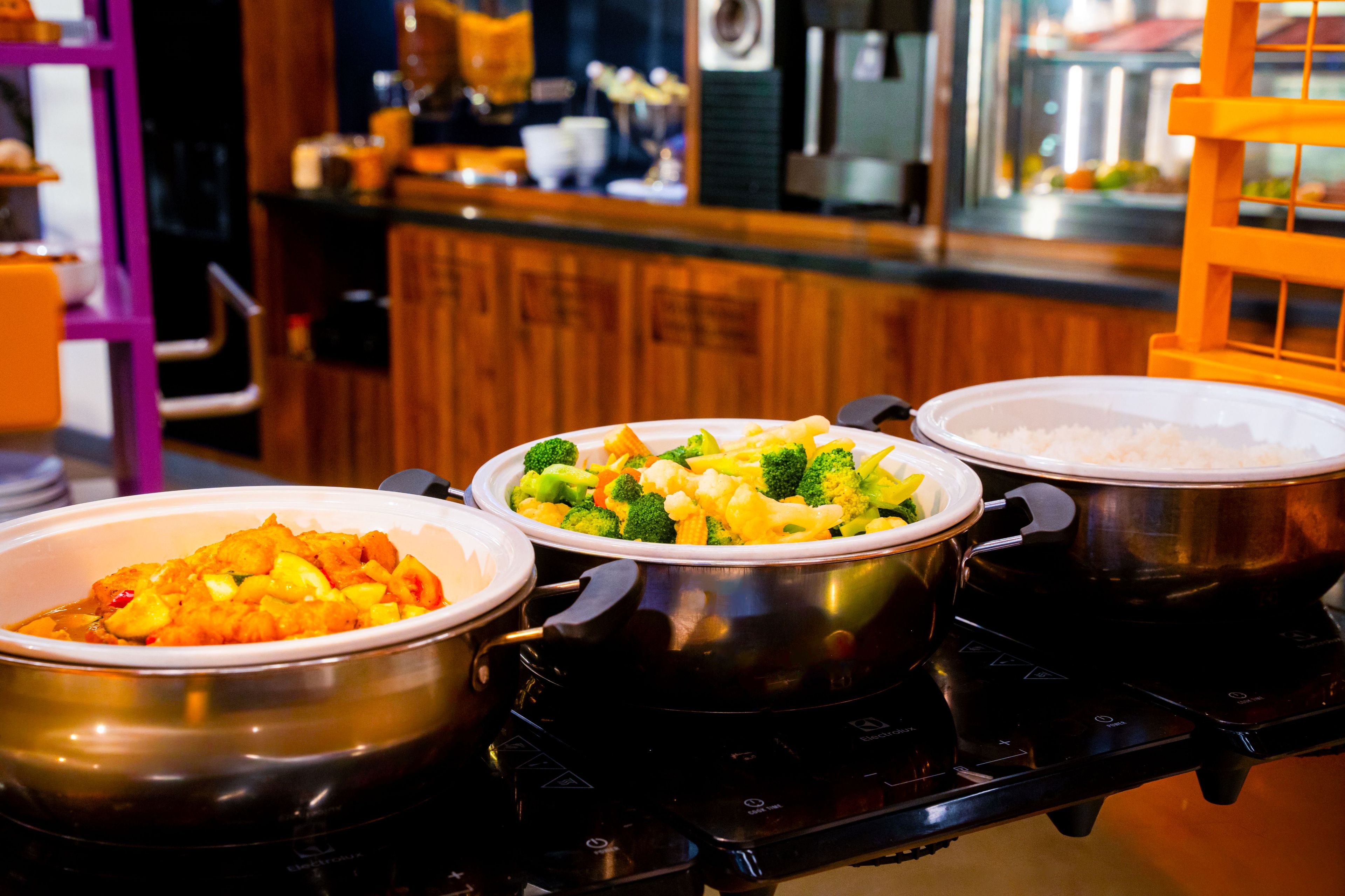 A kitchen with three large pots on a stove, a microwave, and various kitchen utensils.