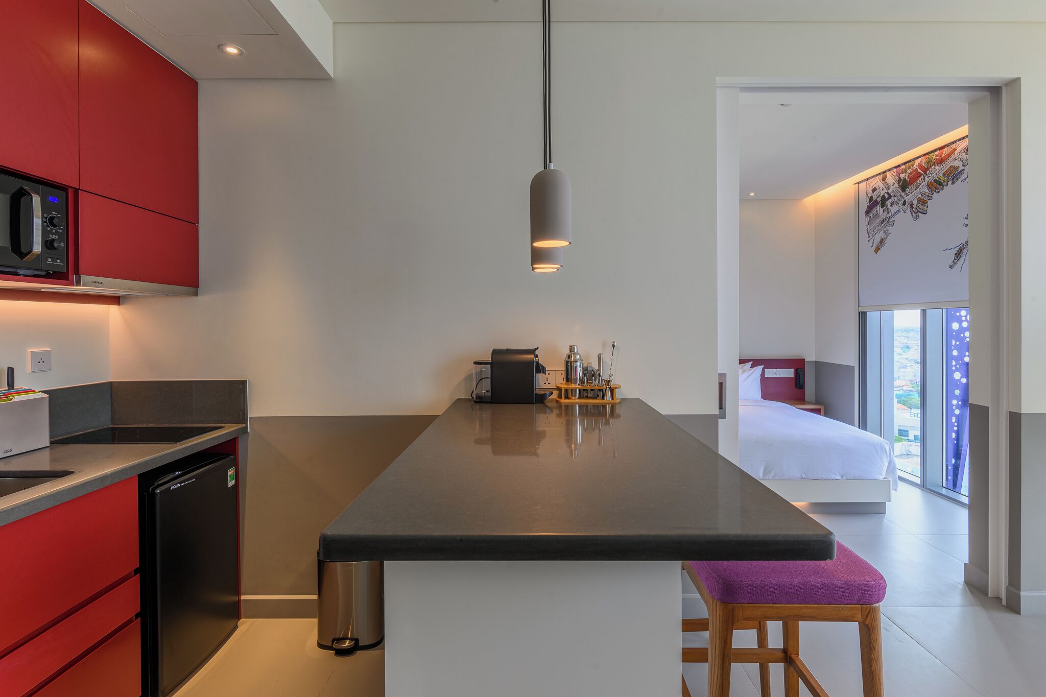 Eine moderne Küche mit einer zentralen Kochinsel, ein Essbereich mit einer Bank und ein Schlafzimmer mit großem Fenster.