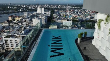 A rooftop pool with the word 'WINK' on the water, surrounded by buildings and a view of a cityscape.