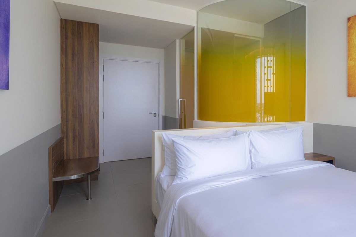 Una habitación de hotel con cama, armario, puerta y un espejo grande.