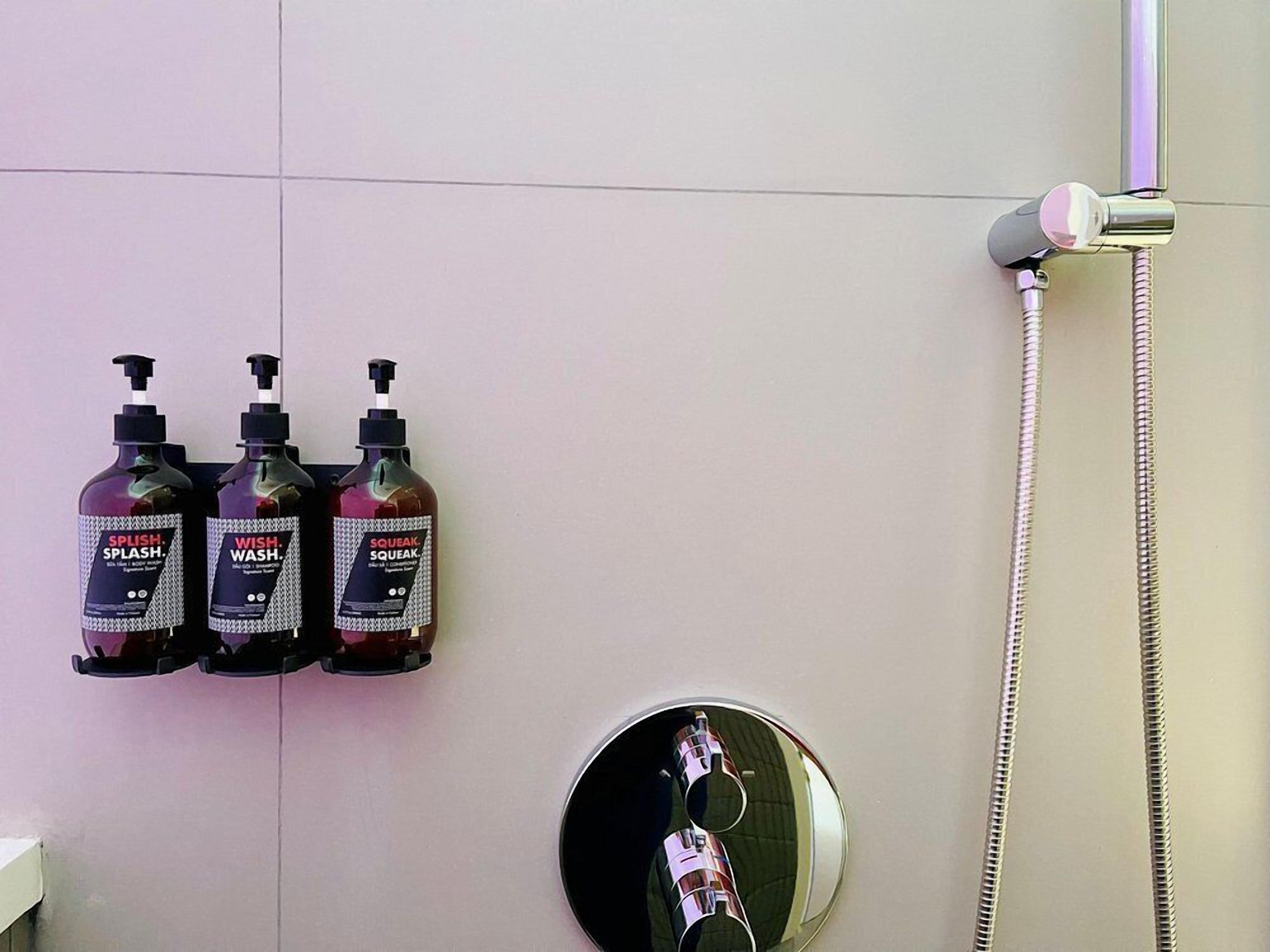 A bathroom with three bottles of soap and a shower head.